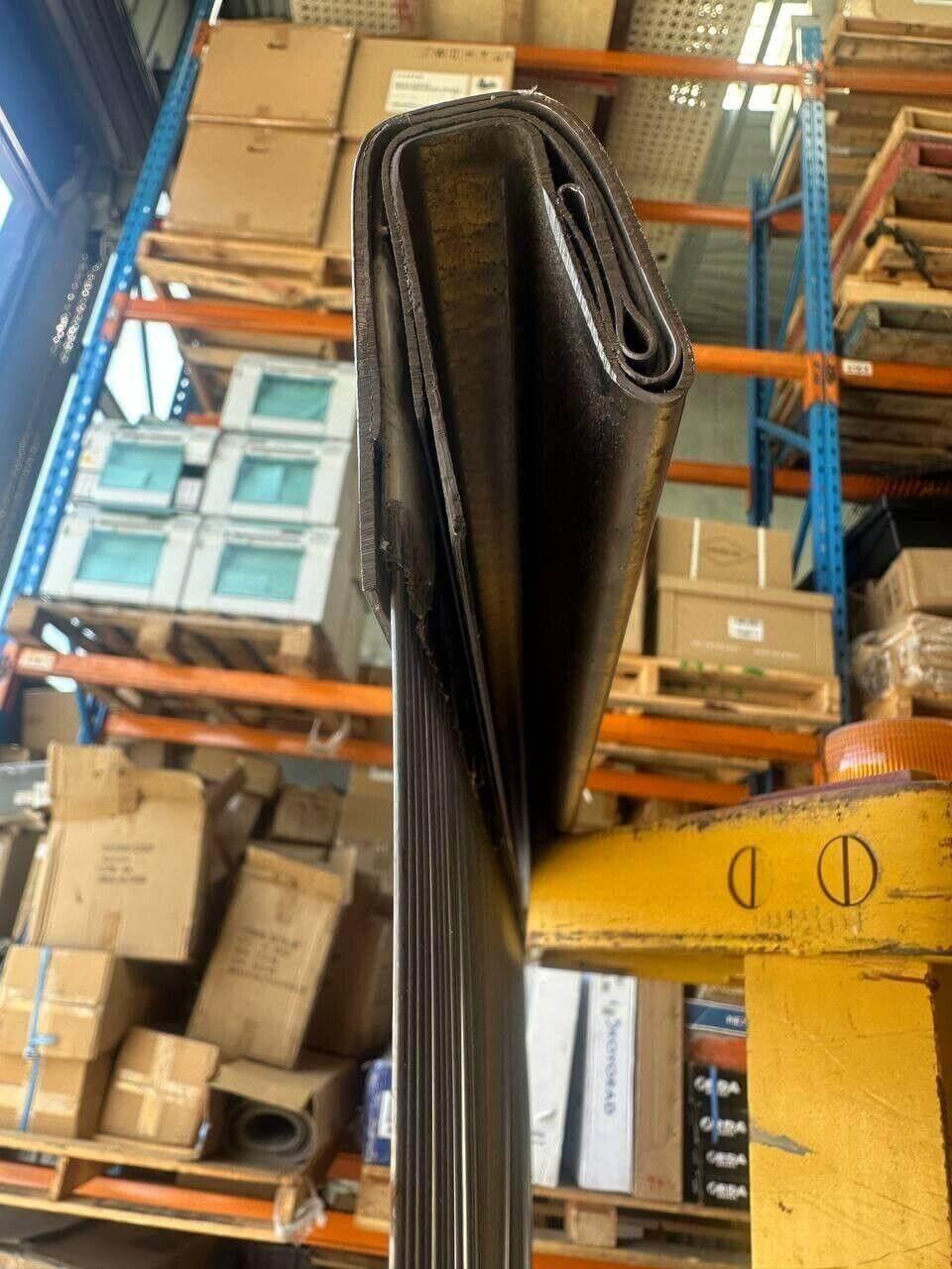 Rolled black tractor belt in warehouse with storage shelves and boxes