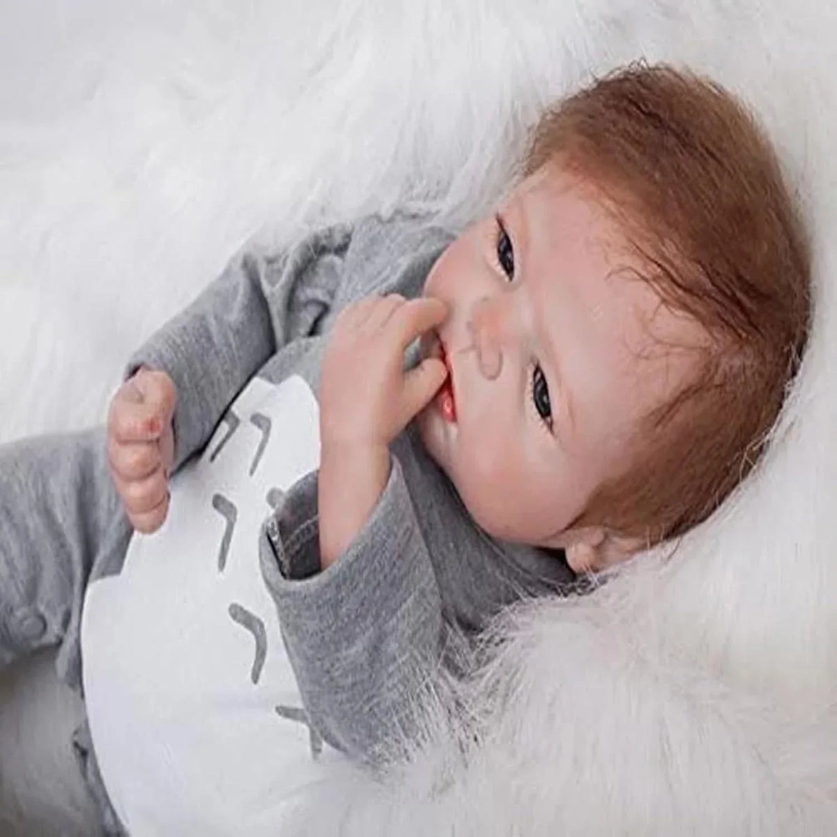 Realistic baby doll with brown hair in gray outfit, lying on white fur