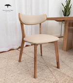 Modern wooden dining chair with cream upholstered seat and back, styled with matching table and rug