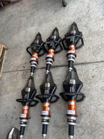 Six Holmatro rescue tools with orange and black design, labeled for inventory on concrete floor.
