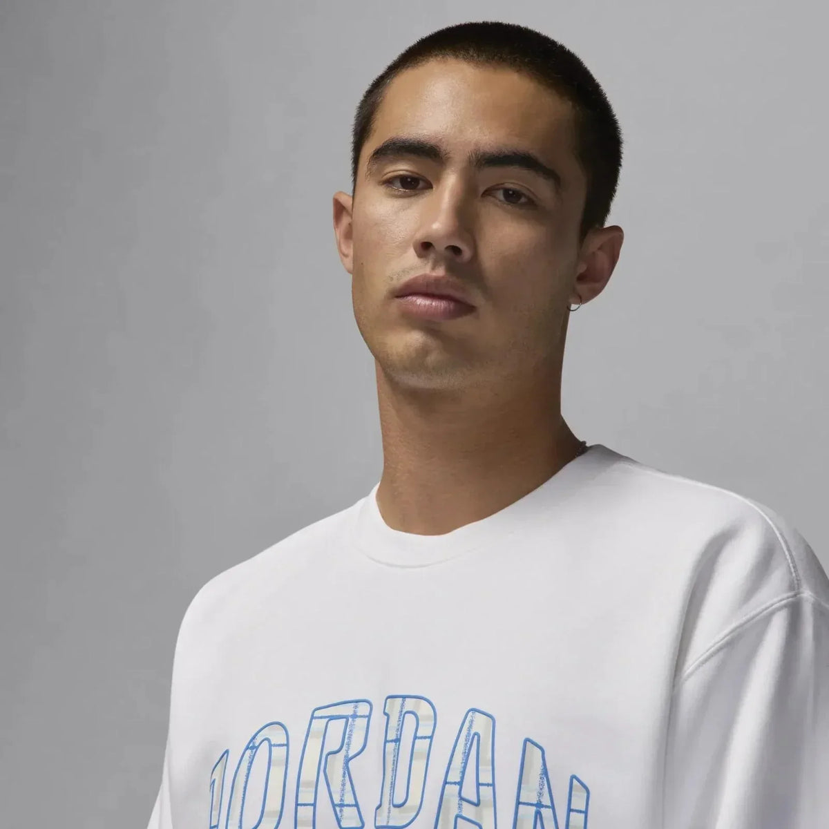 Man wearing white Jordan sweatshirt with blue text, minimalist studio background