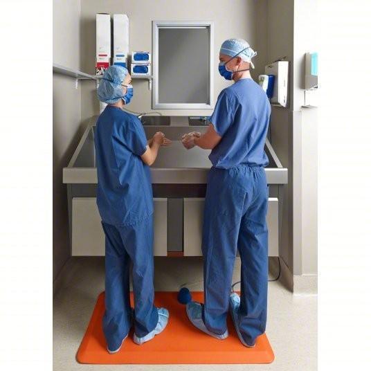 Medical staff in blue scrubs washing hands at sink with orange anti-fatigue mat