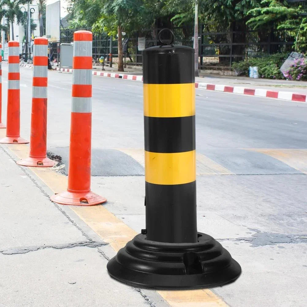 Black and yellow striped traffic bollard with base, orange safety cones on roadside