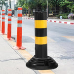 Black and yellow striped traffic bollard with base, orange safety cones on roadside