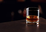 Clear recycled whiskey tumbler with amber liquid on a dark surface