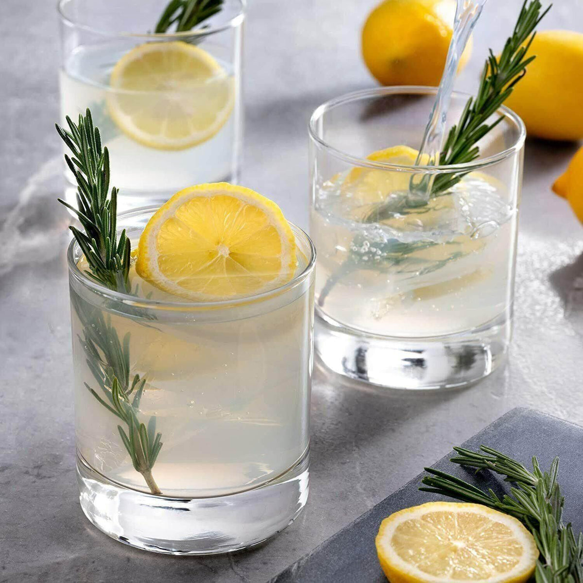 Clear recycled glass tumblers with lemon slices and rosemary, filled with a refreshing drink.