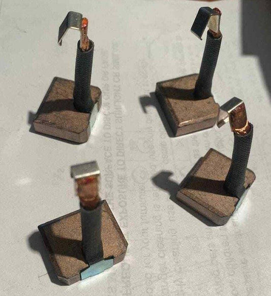 Set of four carbon motor brush blocks with copper connectors on a plain surface