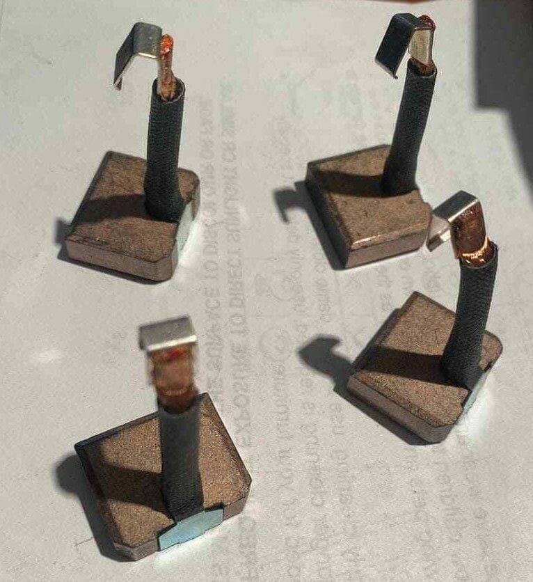 Set of four carbon motor brush blocks with copper connectors on a plain surface