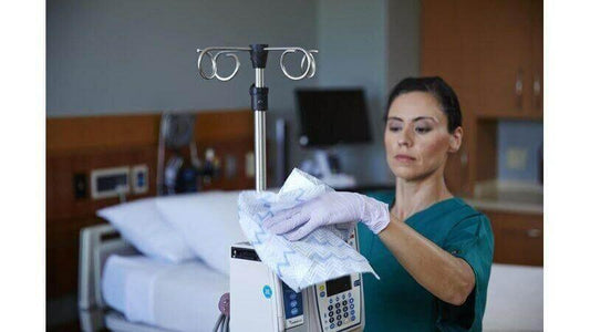 Nurse cleaning medical equipment in hospital room with disposable microfiber cloth