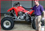 Man maintaining red ATV with engine exposed, using lubricant spray, outdoor garage setting