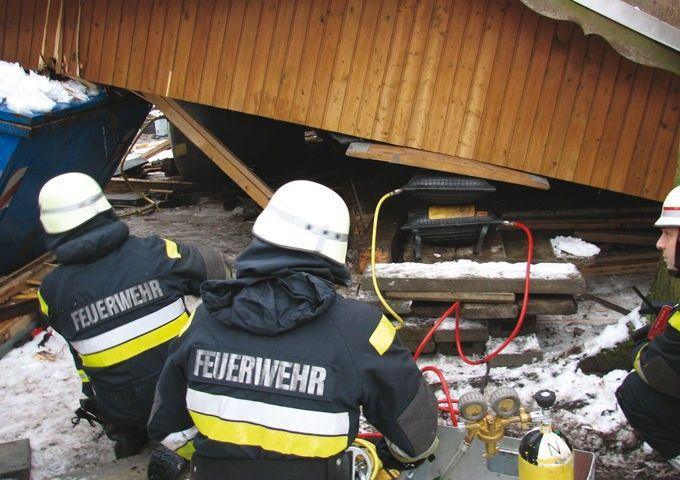 Firefighters in FEUERWEHR gear assessing structural damage at snowy accident scene with rescue equipment