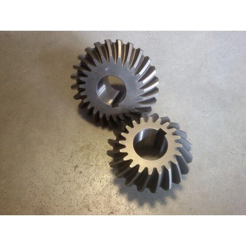 Two metal bevel gears for tractor or machinery parts on a gray surface