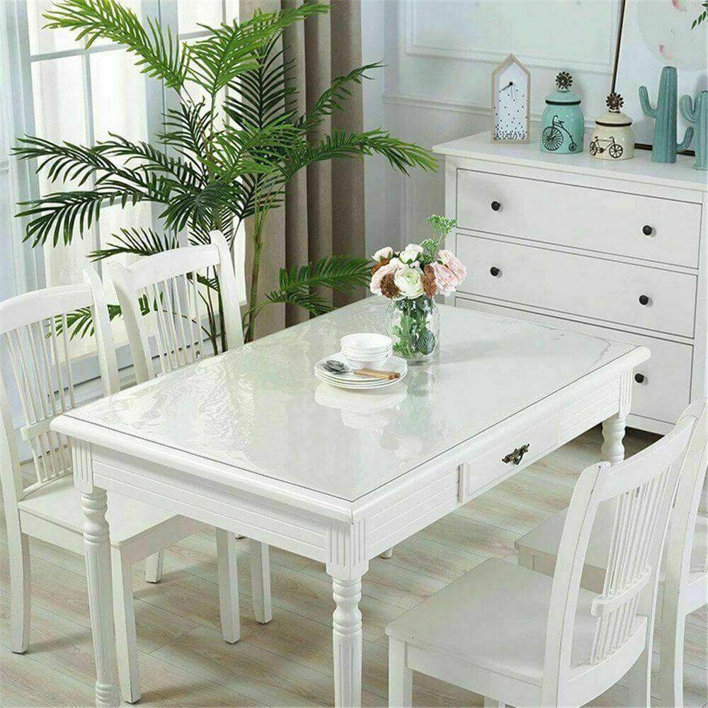 Elegant dining table with clear PVC table cover, surrounded by white chairs and greenery decor.