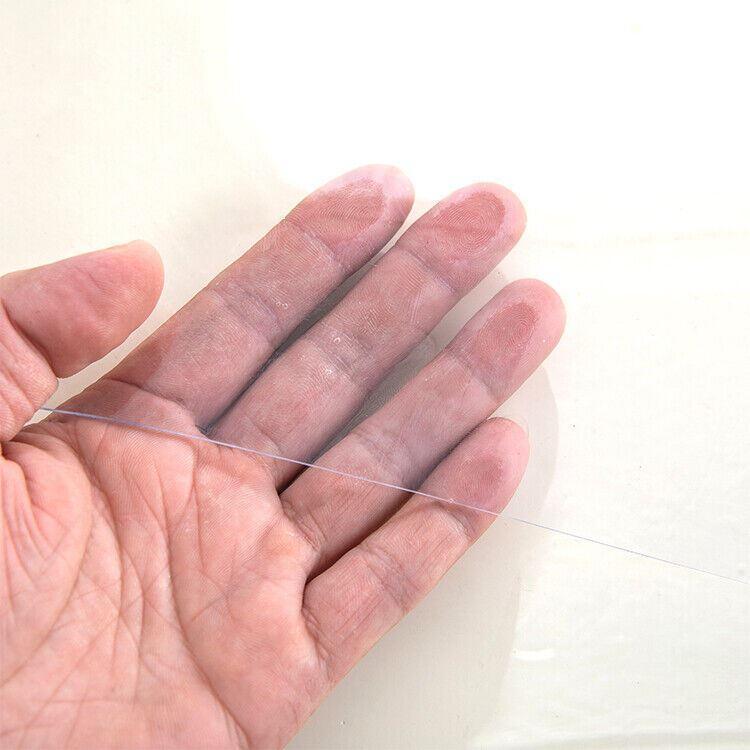 Hand holding a thin, clear PVC table cover, showcasing its lightweight and transparent design for table protection.