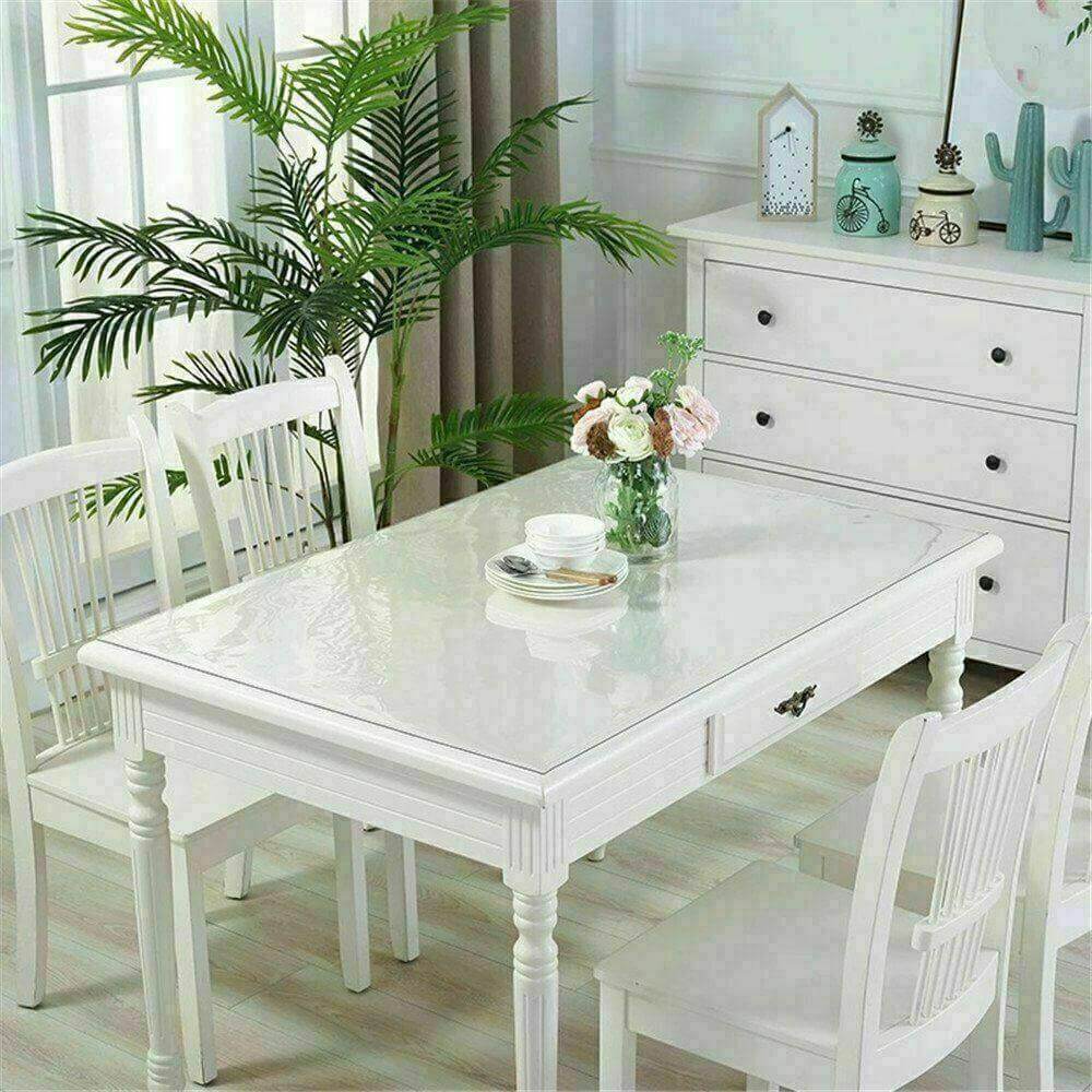 Elegant white dining table with clear PVC cover, surrounded by chairs and decorative plants, showcasing a modern dining space.