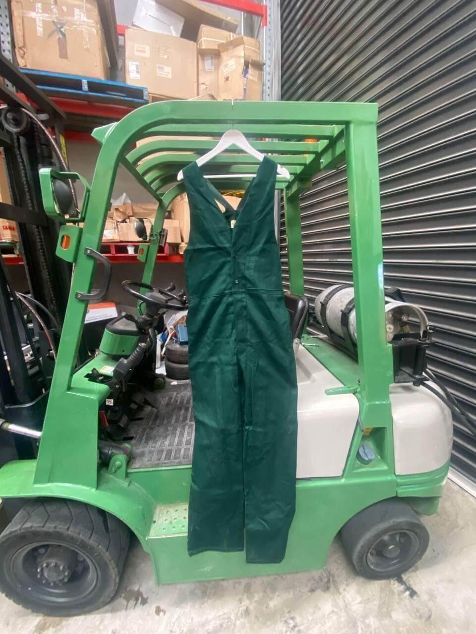 Men's bottle green work overalls hanging on a hanger in an industrial warehouse