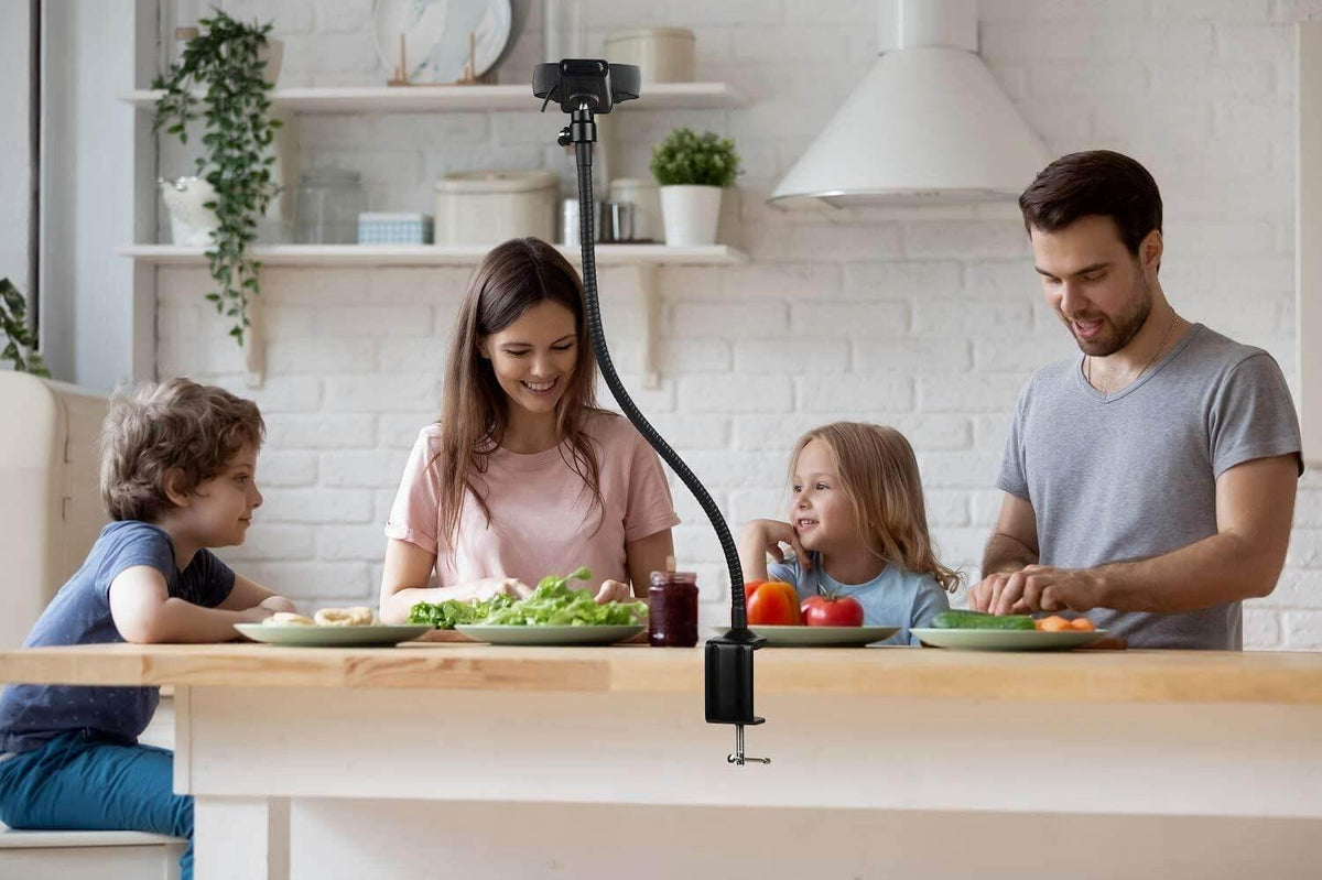 Flexible phone mount on kitchen table with family preparing food, ideal for cooking videos or video calls