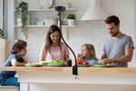 Flexible phone mount on kitchen table with family preparing food, ideal for cooking videos or video calls