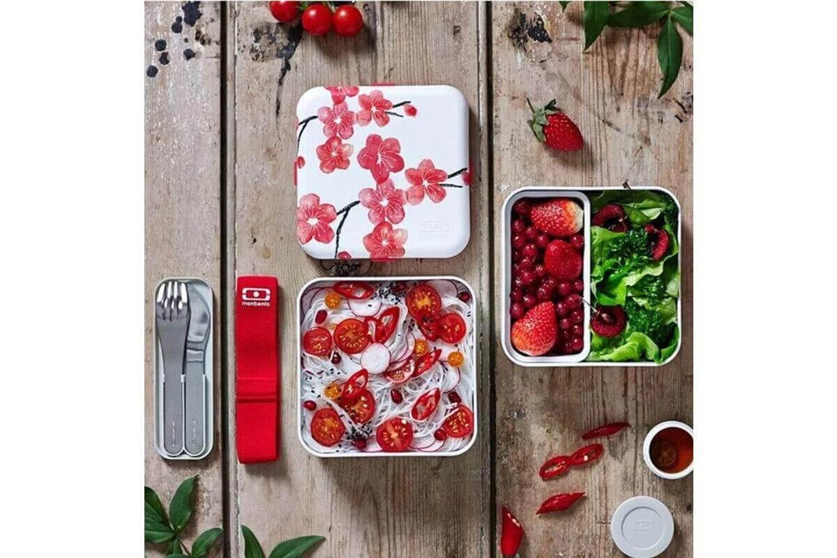 Cherry blossom lunchbox with fresh salad, berries, and utensils on rustic wood