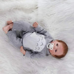 Realistic reborn baby doll in gray onesie with pacifier, lying on white fur blanket