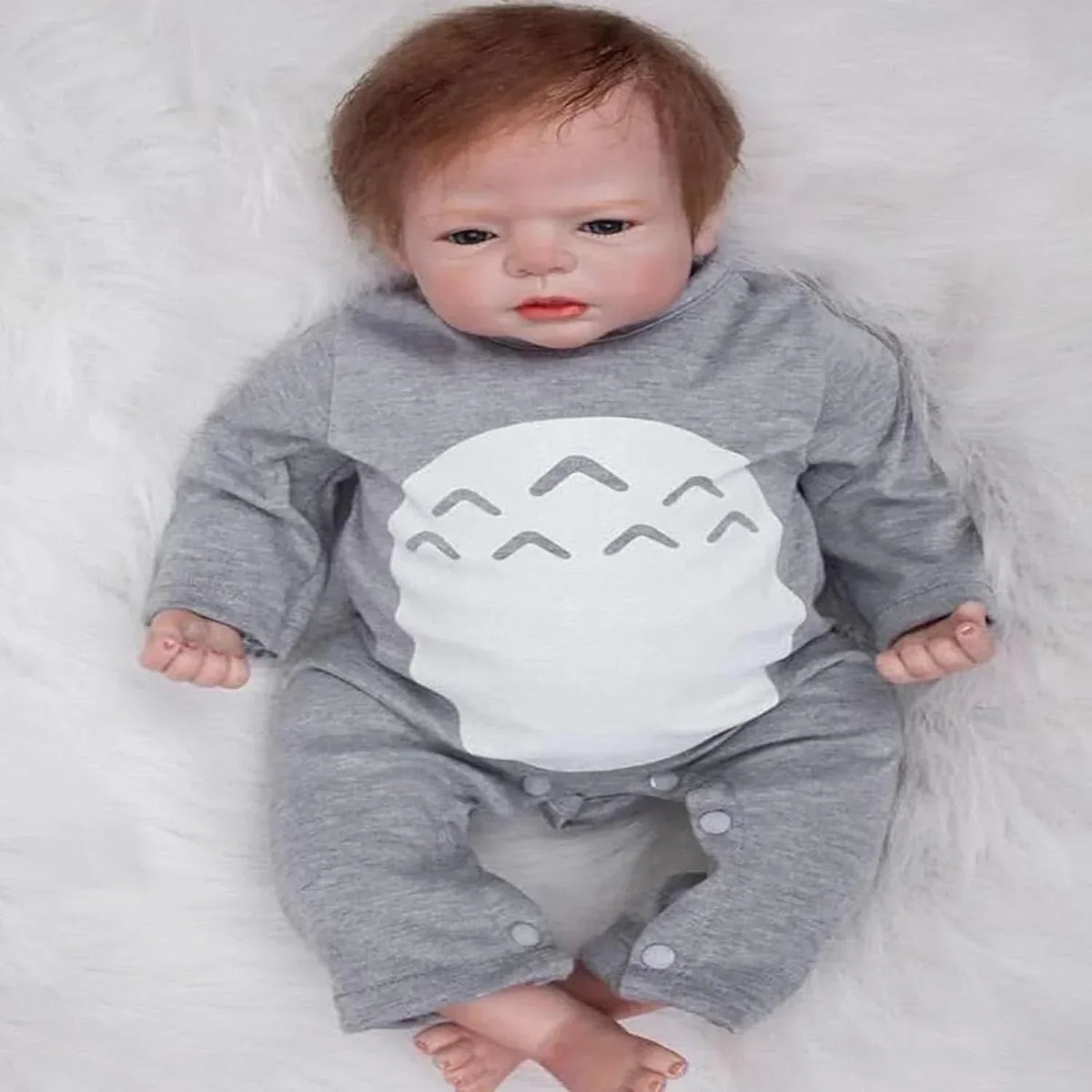 Baby doll in gray onesie with white shark design, lying on soft white surface