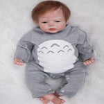 Baby doll in gray onesie with white shark design, lying on soft white surface