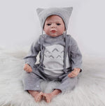 Realistic baby doll in gray cat-themed outfit on fluffy white rug