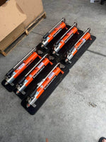 Orange Holmatro hydraulic rescue tools on black trays in warehouse setting