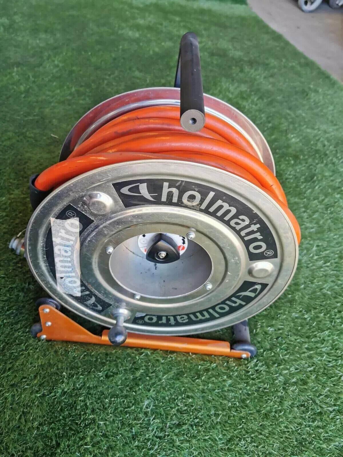 Holmatro hydraulic hose reel with orange hose, metal frame, on artificial grass