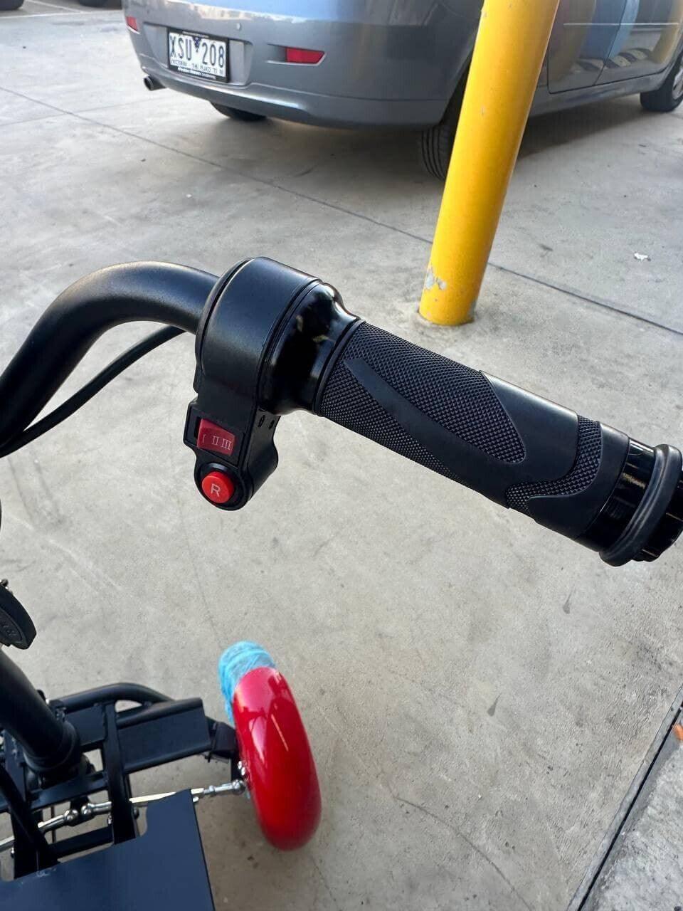 Electric scooter handlebar with red control buttons and black grip, parked near a yellow pole