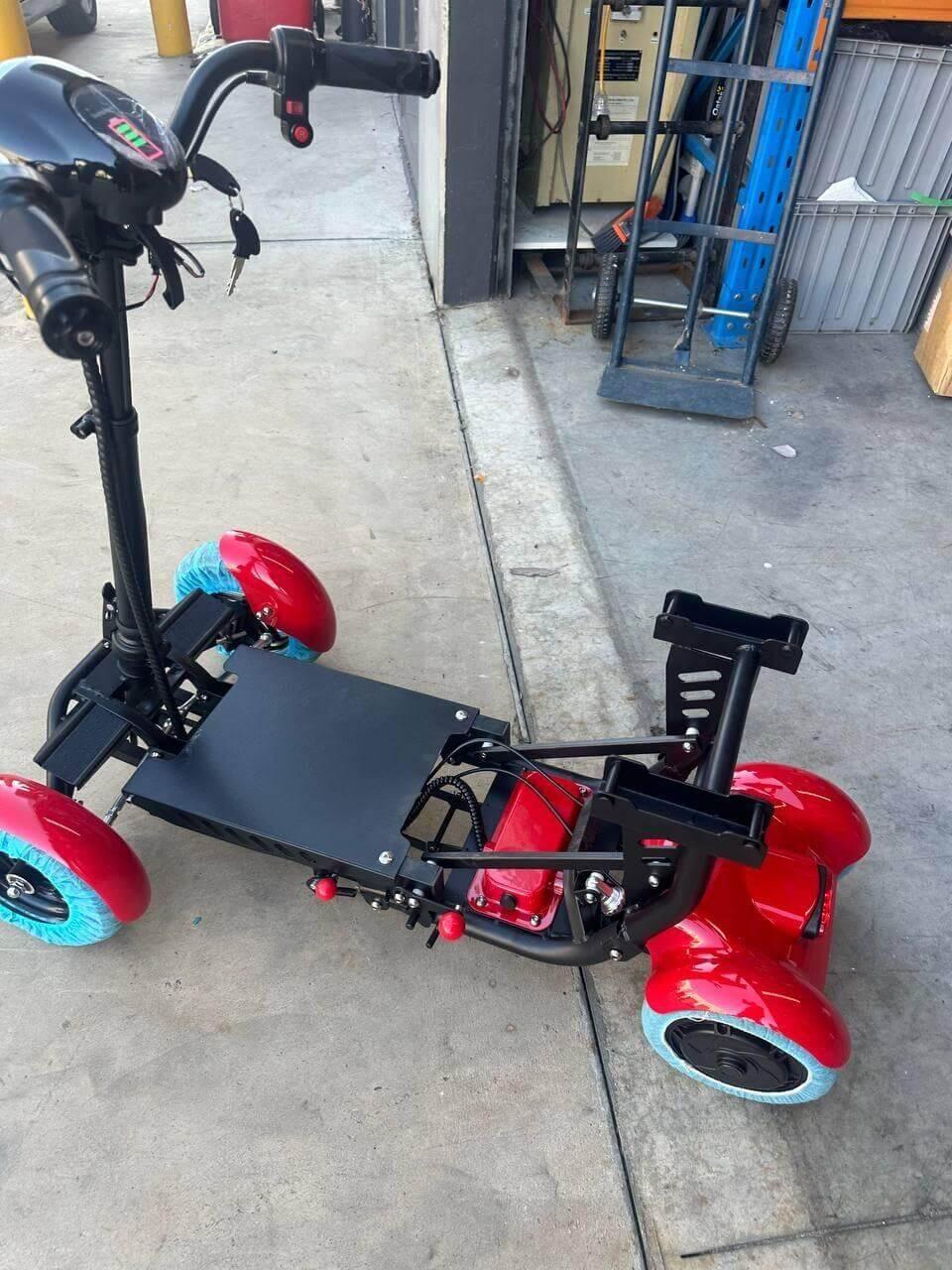 Red electric mobility scooter with blue wheels, parked on concrete near storage area