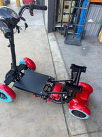 Red electric mobility scooter with blue wheels, parked on concrete near storage area