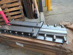 Industrial metal tractor parts with bolts, resting on cardboard in warehouse