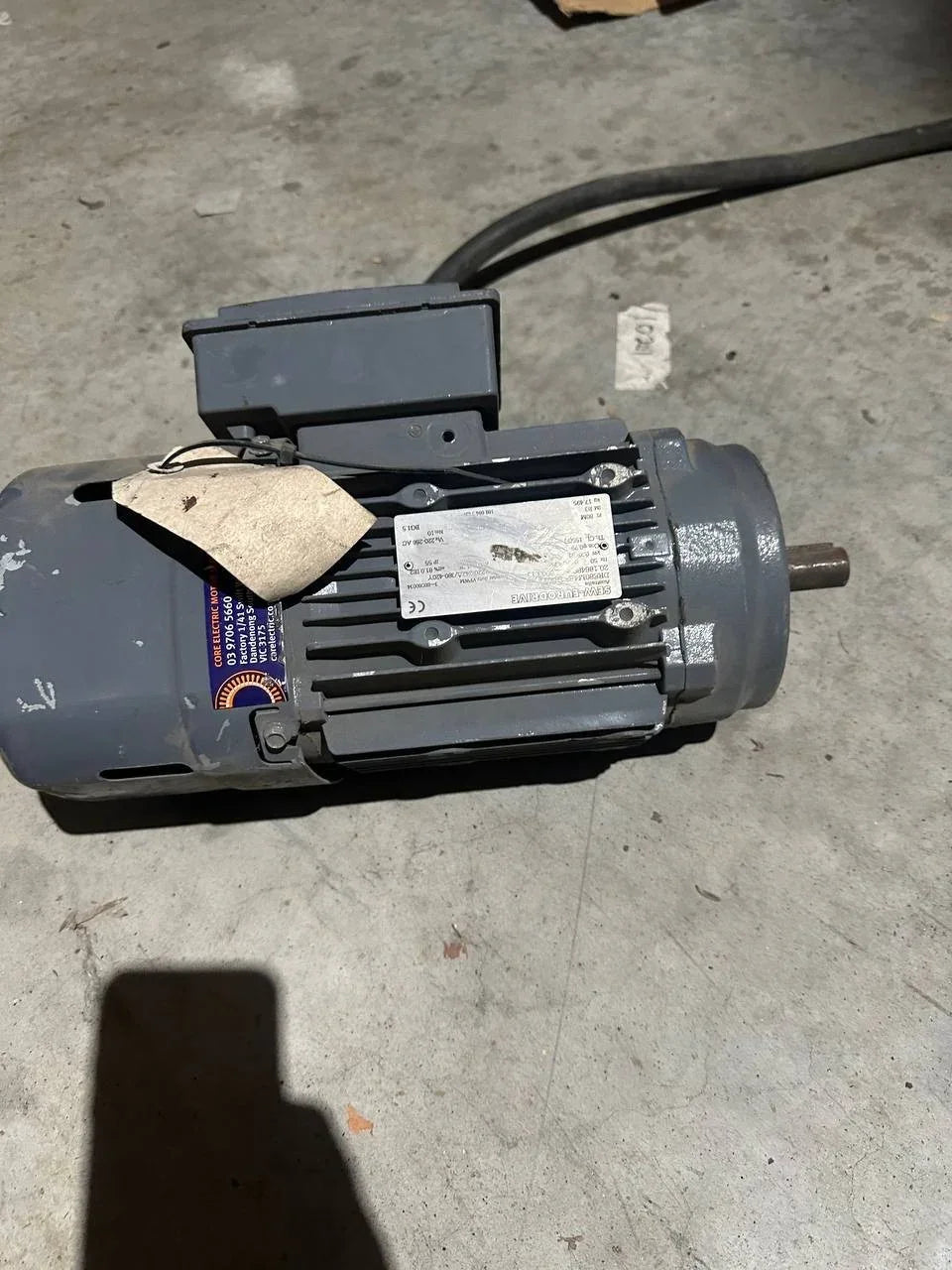 Industrial electric motor with label, suitable for tractor or machinery parts, resting on concrete floor
