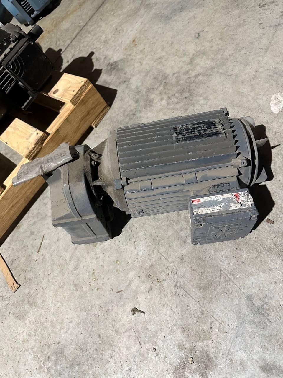 Industrial electric motor with ribbed casing, mounted on concrete floor, suitable for tractor or truck parts