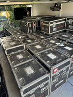 Stacked black road cases for stage lights, labeled '700 wash' and 'atomics w scrollers', in storage
