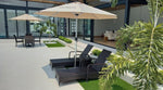 Outdoor patio with wicker lounge chairs, beige umbrellas, and greenery near modern glass doors