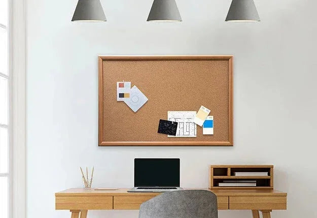 Wooden desk with corkboard, laptop, and office supplies in a bright workspace