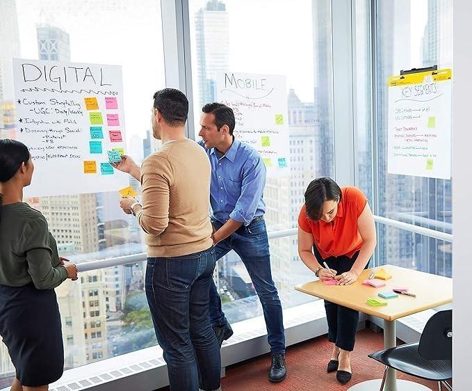 Team brainstorming with sticky notes on whiteboards in modern office with city view