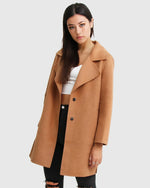 Women's camel coat with double buttons, paired with white top and ripped black jeans