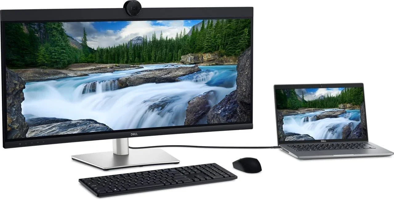 Dell monitor and laptop setup with keyboard, mouse, and scenic waterfall display