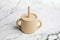 Beige toddler sippy cup with straw and dual handles on marble surface