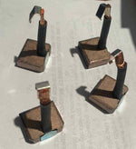 Set of four carbon motor brush blocks with copper connectors on a plain surface