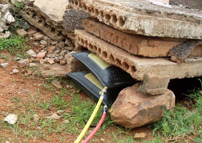 Black tractor tire under concrete blocks with yellow and red hoses connected outdoors