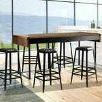 Set of four industrial bar stools with black metal legs and leather seats around a wooden dining table in a modern kitchen