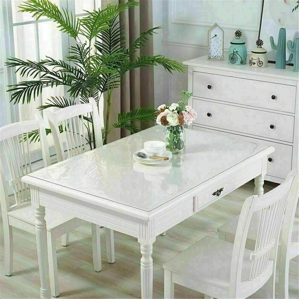 Elegant white dining table with clear PVC cover, surrounded by chairs and decorative plants, showcasing a modern dining space.